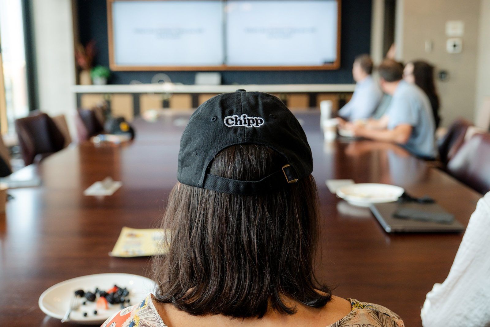 An attendee in a Chipp hat watches a session from the conference table