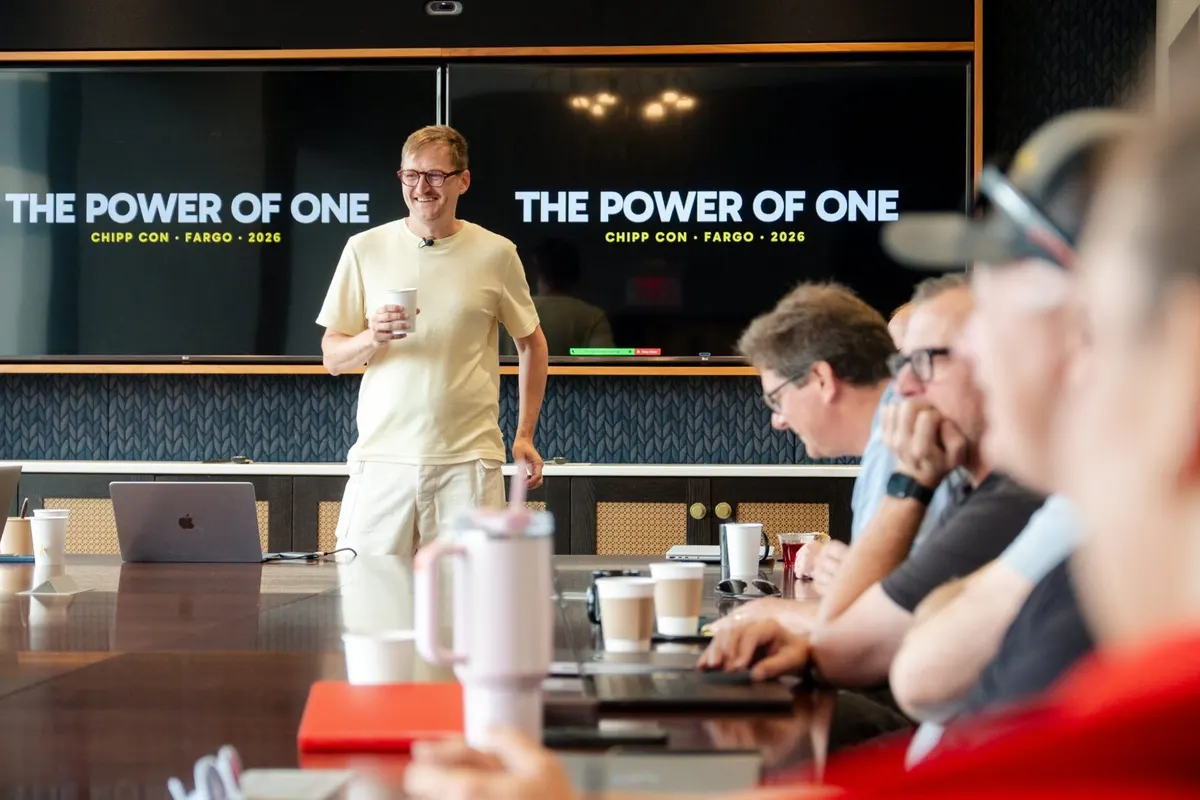 A Chipp Con speaker smiles at the room in front of a The Power of One slide